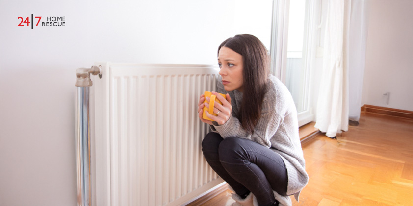 Girl squatting by radiator with a cup of hot tea to keep warm