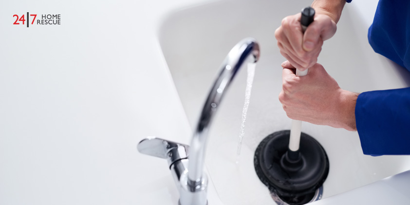 Person in blue uniform using a plunger on a sink with a chrome faucet and running water