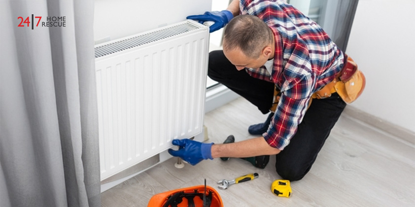 Technician in work overalls using a wrench to repair a heating radiator in a room
