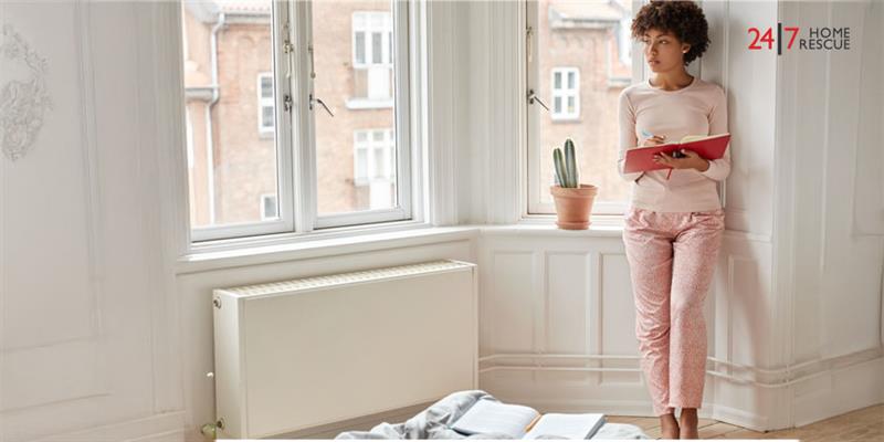 Woman standing by radiator and window with notebook