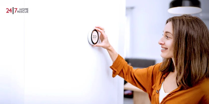 A young woman regulates the heating temperature with a modern wireless thermostat installed on the white wall at home