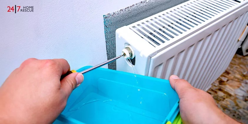A man is bleeding a radiator with a screwdriver