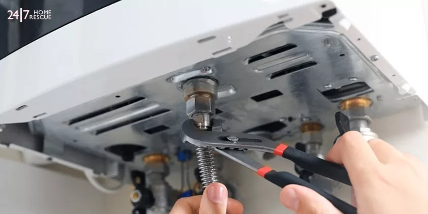 A person using a wrench to tighten a nut on the underside of a boiler