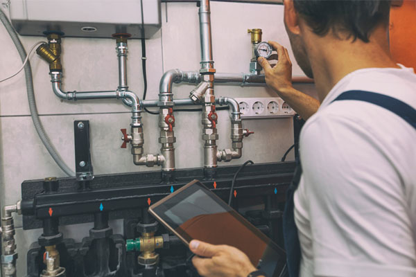 The technician checking the heating system in the boiler room with tablet in hand