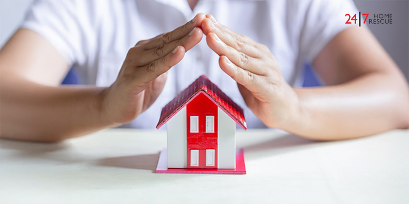 A person's hands forming a protective gesture over a small model house on a table