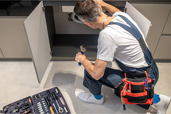 Plumber repairing pipes under a kitchen sink with a wrench.