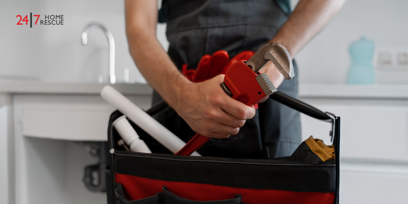 Technician holding red pipe wrench standing by sink with plumbing tools