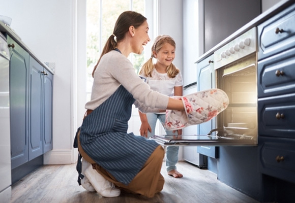 Woman and child using oven mitts to remove tray – Oven Insurance
