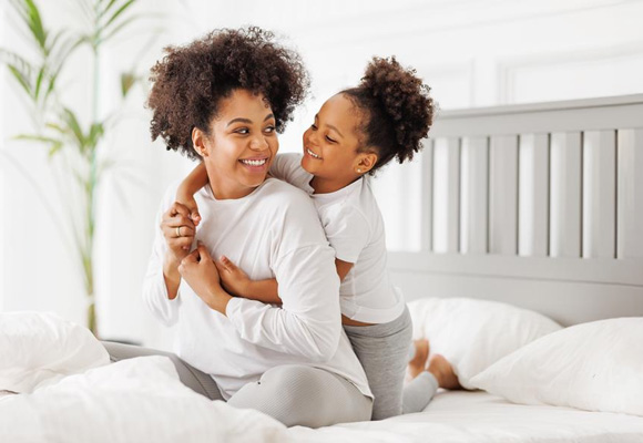 Mother and daughter hugging and smiling on a bed in a warm home
