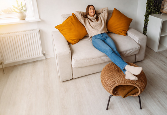 Woman relaxing on sofa with feet up near radiator in warm home